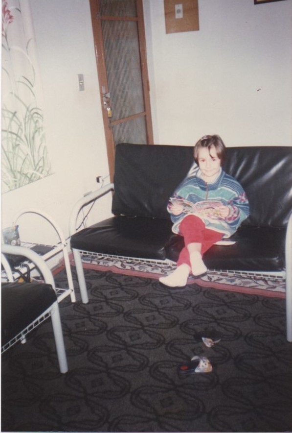 Criança sentada em um sofá, com as pernas cruzadas e com um gibi aberto nas mãos.