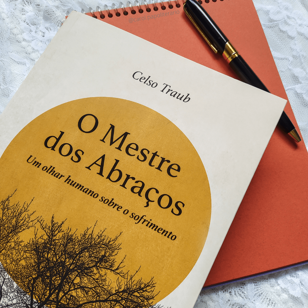 Livro O Mestre dos Abraços em primeiro plano, apoiado em um bloco de anotações sem pauta, com uma caneta elegante em cima do bloco.