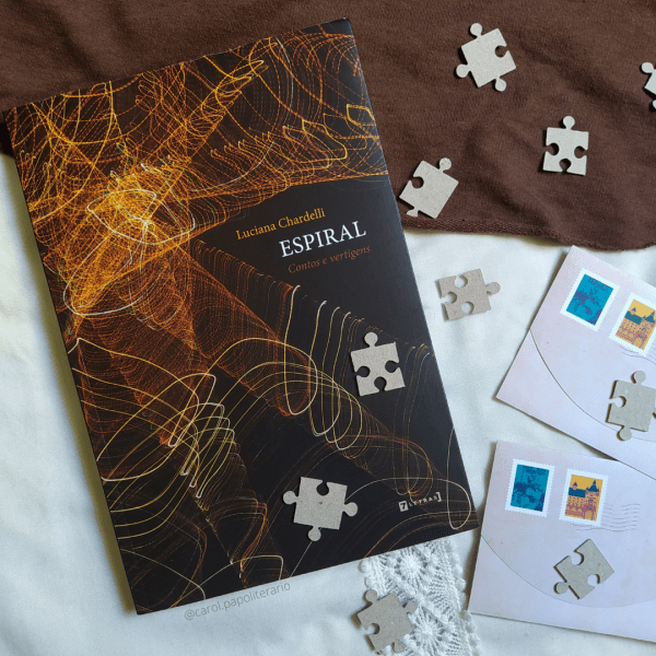 Livro Espiral, com dois envelopes de carta ao lado, no canto inferior direito da imagem, e peças de quebra-cabeça espalhados pela imagem.