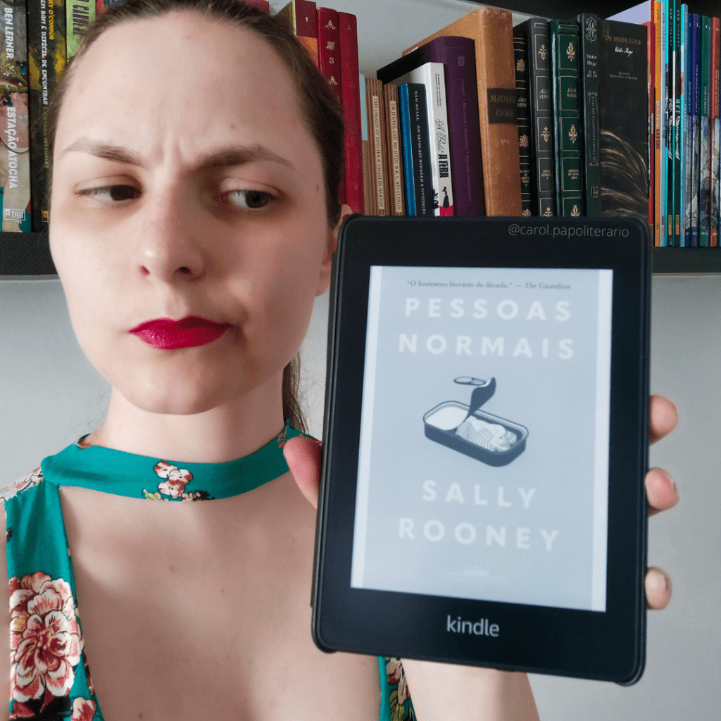 Moça olhando para um kindle com a capa do livro Pessoas Normais. Ela está com o cenho franzido e a boca contraída, em expressão de desagrado.