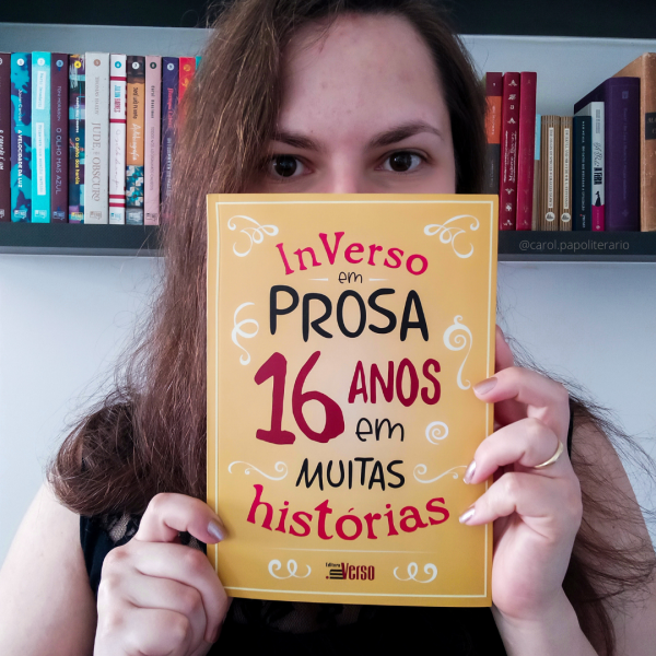 Carol mostrando o livro "InVerso em Prosa, 16 anos em muitas histórias" em frente ao rosto.