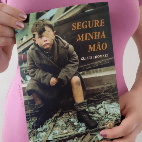 Carol mostrando o livro Segure Minha Mão, segurando o objeto na altura da cintura.