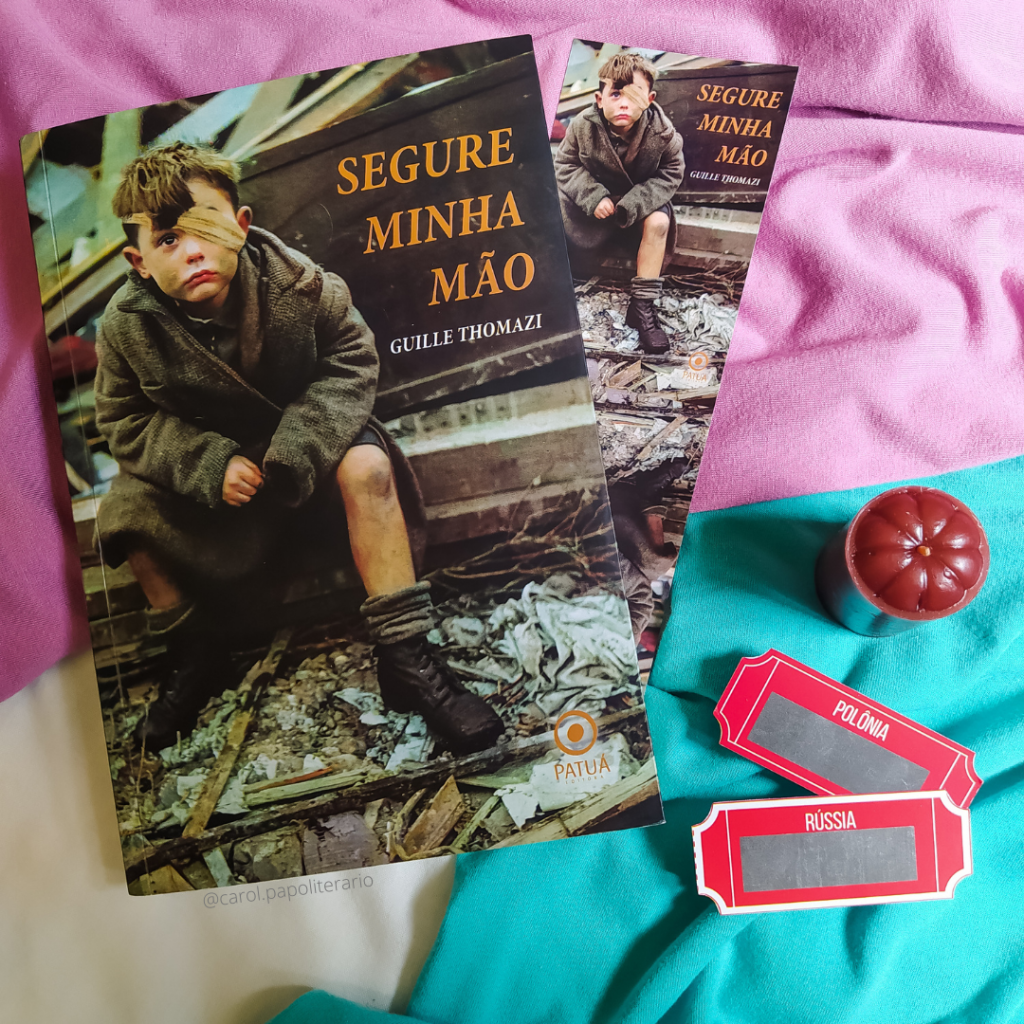Livro Segure Minha Mão, com um marcador com a capa do livro ao lado. Há uma vela e duas imitações de ticket de trem ao lado do livro. Em um dos tickets está escrito "Polônia" e no outro, "Rússia".
