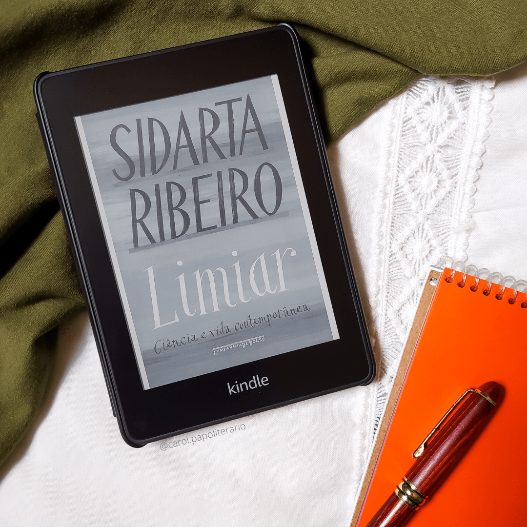 Kindle com a capa do livro Limiar, com um bloco de anotações com uma caneta apoiada em cima à esquerda do Kindle.