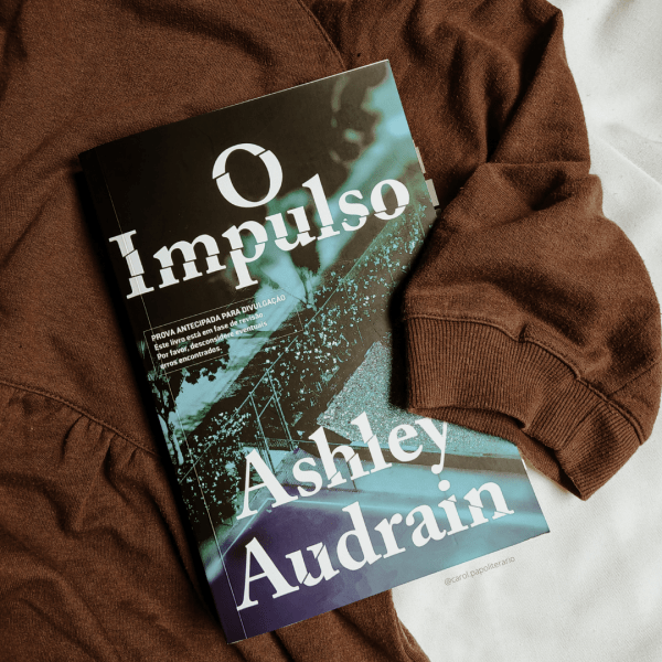 Livro O Impulso, envolto por uma blusa de manga curta, como se estivesse sendo abraçado.