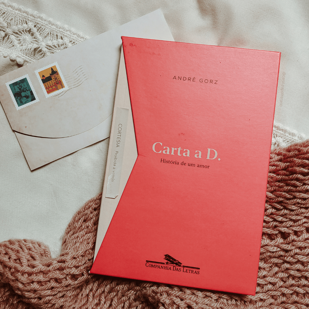 Livro Carta a D em evidência, dentro do box que imita um envelope. Há um envelope de carta com desenhos de selo aparecendo por baixo do livro.