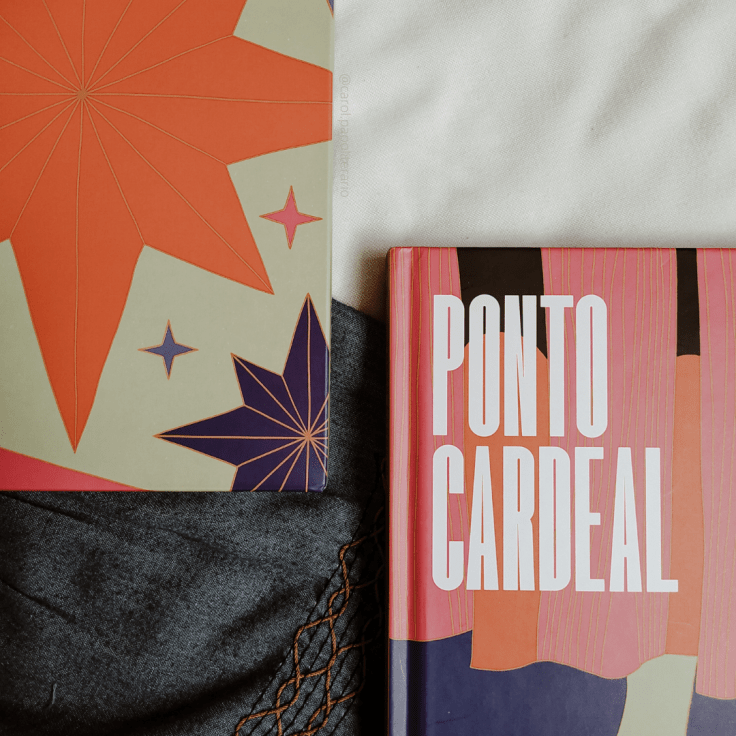 Livro Ponto Cardeal, em edição do clube de assinaturas TAG, no canto inferior direito da imagem, mostrando apenas uma parte do livro, onde se lê o título. No canto superior direito, está a luva da edição, com desenhos de rosa dos ventos.