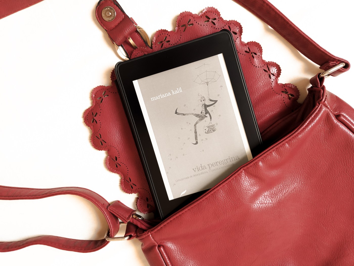 Kindle com a capa do livro "vida peregrina" saindo de uma bolsa de passeio aberta.