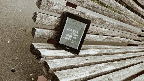 Kindle com a capa do livro Cartas para Minha Avó em cima de um banco de madeira